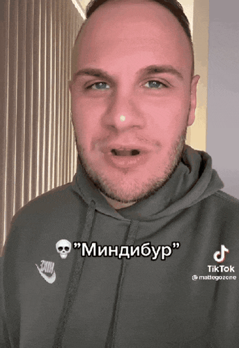 a man wearing a grey nike hoodie has a skull on his sweatshirt