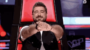a man with a beard is sitting in a chair with his eyes closed and his hands folded .