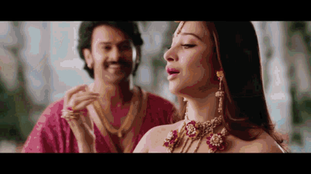 a man and woman are standing next to each other and the woman is wearing a necklace and earrings .