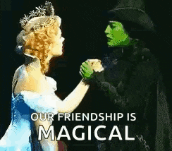 a woman in a blue dress and a green woman in a black top hat are holding hands on a stage .