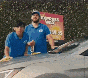 two men standing next to a car in front of a express wax sign