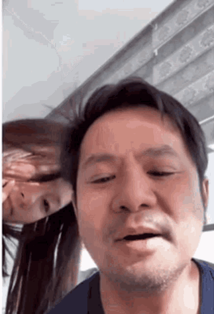 a man with a beard is making a funny face while a woman looks over his shoulder .