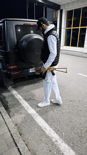 a man is standing in front of a black mercedes holding a gun