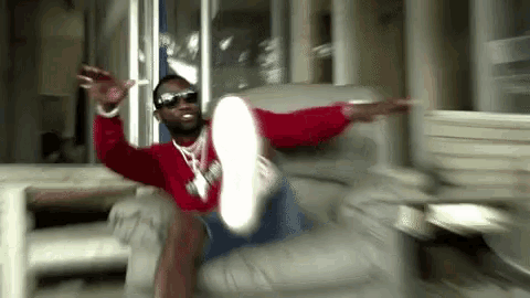 a man wearing sunglasses and a red sweatshirt is sitting on a couch with his feet up .