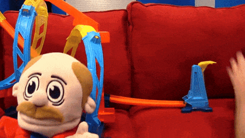 a puppet is sitting on a red couch next to a toy track
