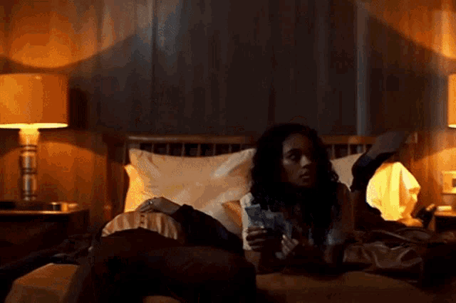 a woman is laying on a bed holding a glass of water