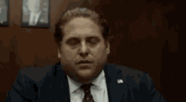 a man in a suit and tie is sitting at a table with his eyes closed and his hand on his face .