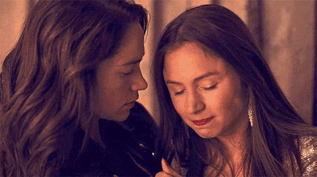 two women are touching each other 's faces and one has red lipstick on