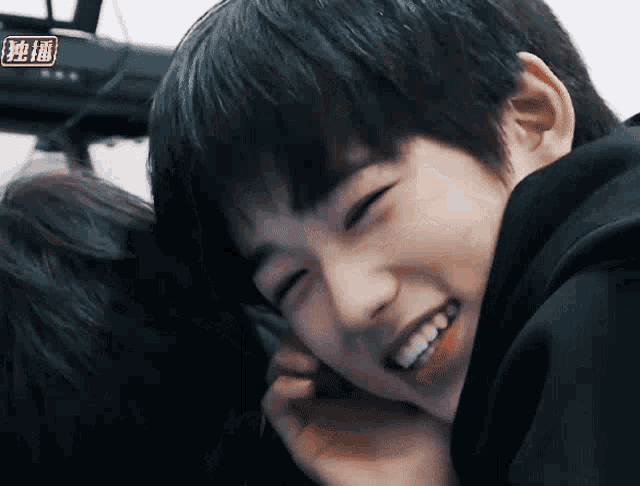 a young boy is smiling and talking on a cell phone while sitting next to another boy .