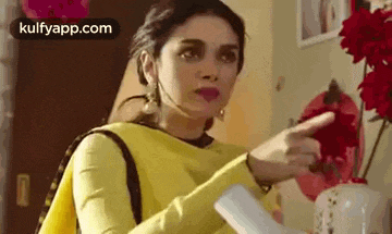 a woman in a yellow dress is pointing at something while sitting at a table .
