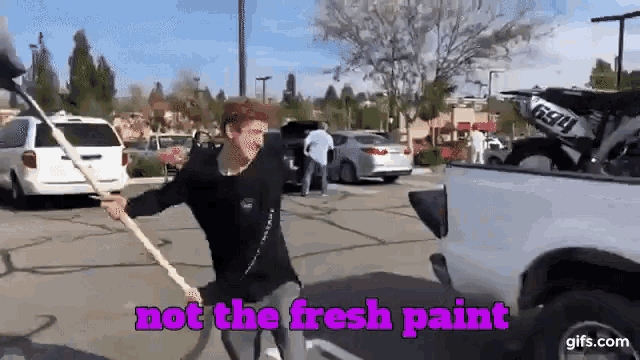 a man holding a stick in a parking lot with the words " not the fresh paint "