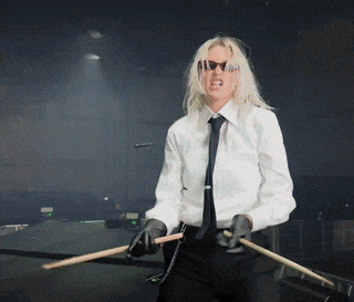 a woman in a white shirt and tie is holding a drum stick