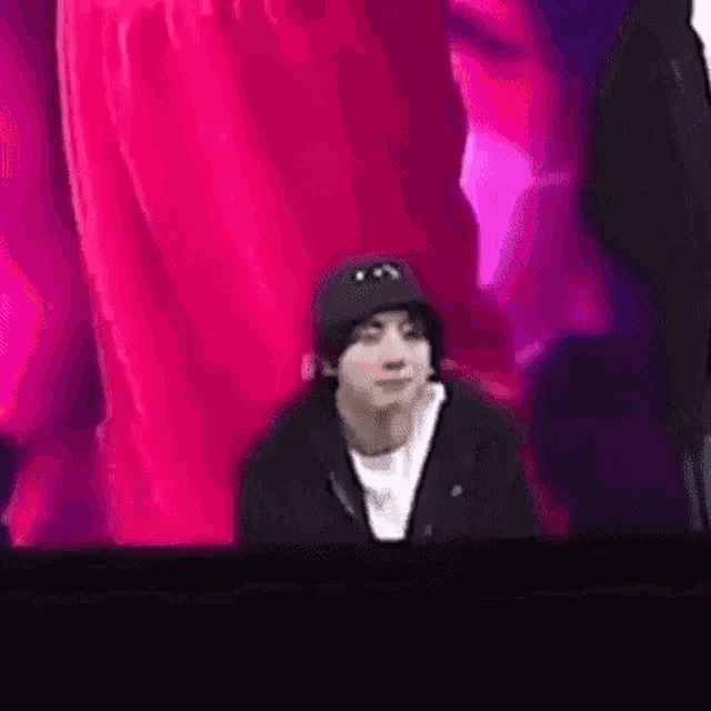 a man wearing a black hat is sitting in front of a pink background .
