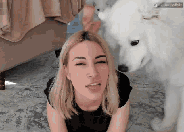 a woman laying on the floor with a white dog looking at her face .