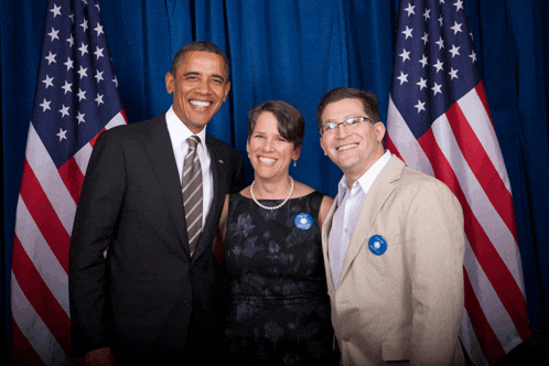 two men and a woman pose for a picture in front of an american flag