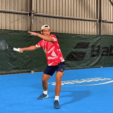 a man is playing tennis on a blue court with a babolat banner behind him
