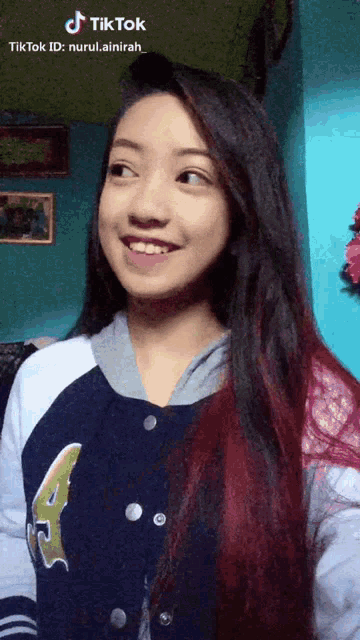 a girl with long red hair is smiling and wearing a blue and white jacket with the number 4 on it