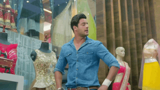 a man in a denim shirt stands in front of mannequins in a store