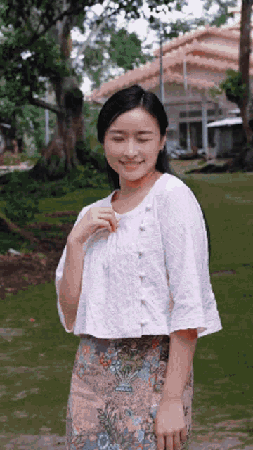 a woman wearing a white top and a floral skirt is smiling