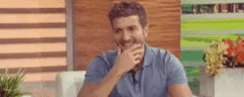 a man in a blue shirt is sitting on a couch with his hand on his chin .