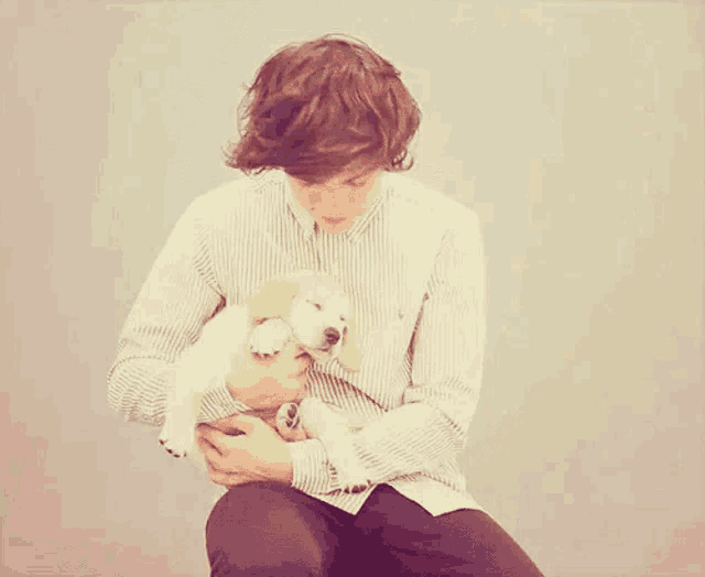 a man in a striped shirt is holding a small puppy