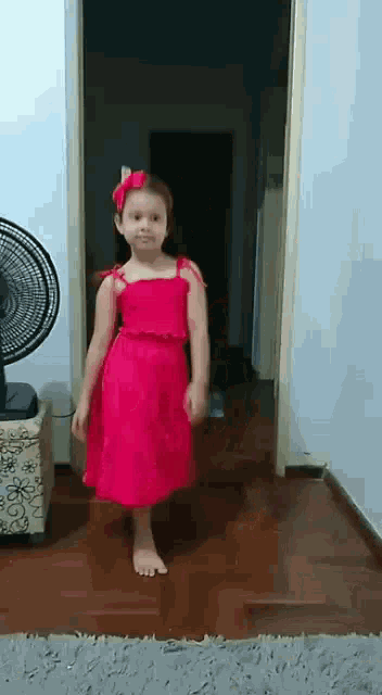 a little girl in a red dress is standing in front of a fan in a room .