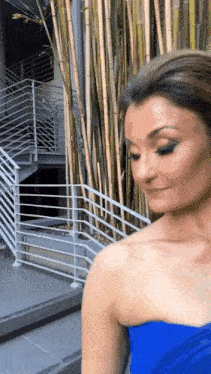 a woman in a blue strapless dress is standing in front of a building with stairs .