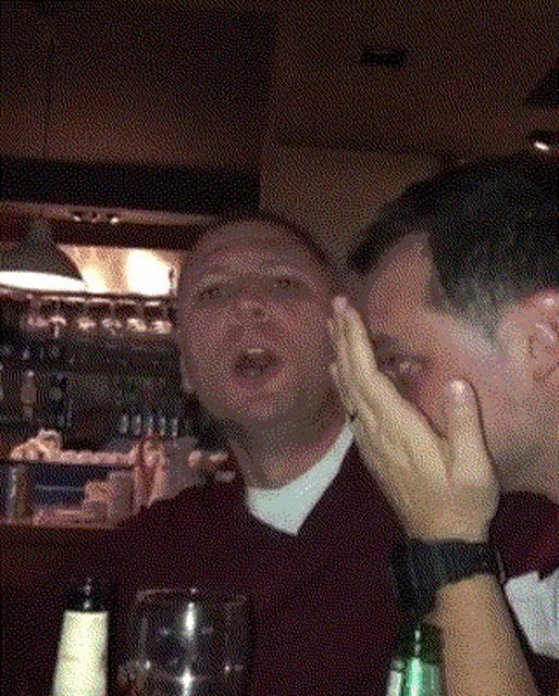 a man covering his face with his hand while another man laughs