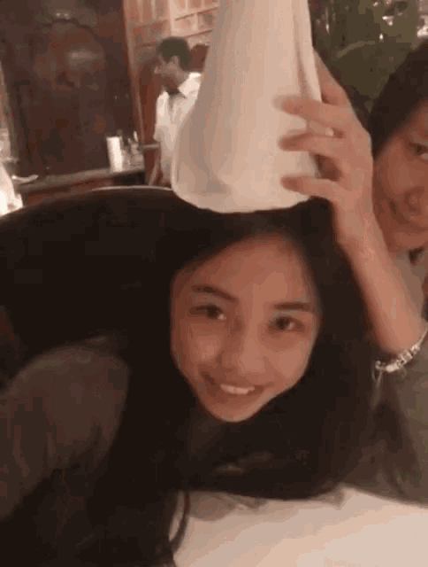 a woman is sitting at a table with a man holding a pizza on her head .