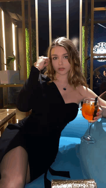 a woman in a black dress holding a glass of orange liquid