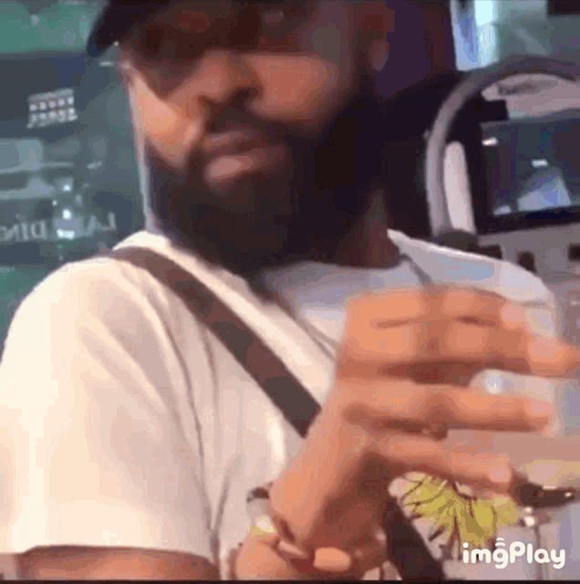 a man with a beard is wearing a white shirt and a hat while holding a glass of water .