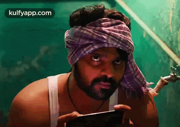 a man wearing a turban is holding a cell phone .