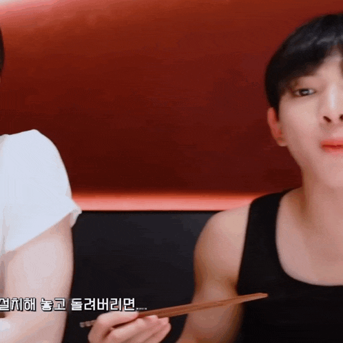 a man in a black tank top is holding chopsticks