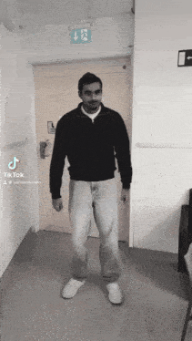 a man is standing in front of a door with a tiktok logo on the bottom right