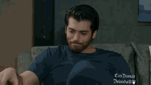 a man is sitting on a couch wearing a blue shirt that says can yaman