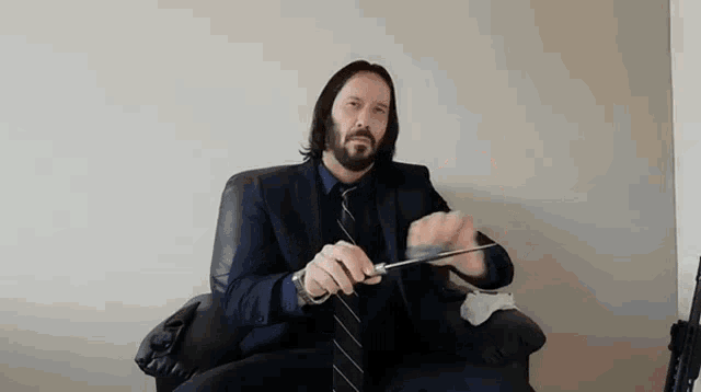 a man with a beard is sitting in a chair holding a pair of scissors .