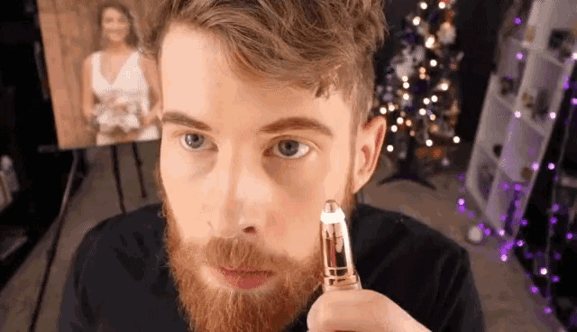 a man with a beard is using a hair remover to remove his eyebrows .