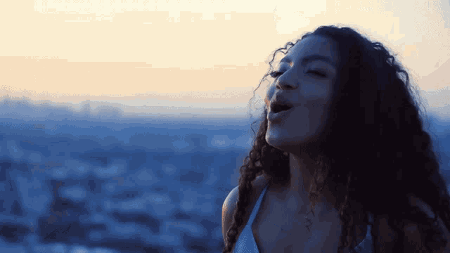 a woman with curly hair is singing in front of a blue sky