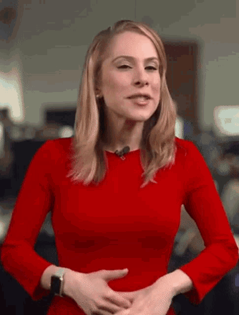 a woman in a red dress is standing in front of a microphone and holding her hands on her stomach .