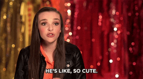 a woman is standing in front of a red curtain and says he 's like , so cute .