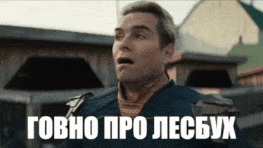 a man with a surprised look on his face is standing in front of a building with russian writing on it