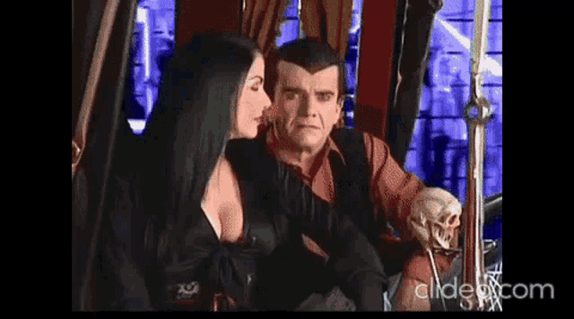 a man and a woman are sitting next to each other . the woman is holding a skull .