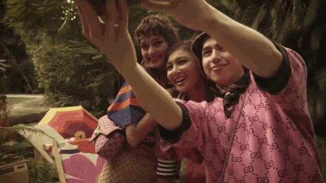 a woman in a pink gucci shirt is taking a selfie with two other women