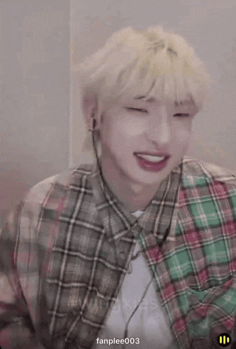 a young man wearing a plaid shirt and earbuds smiles for the camera