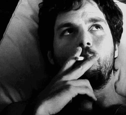 a man with a beard is smoking a cigarette in a bed