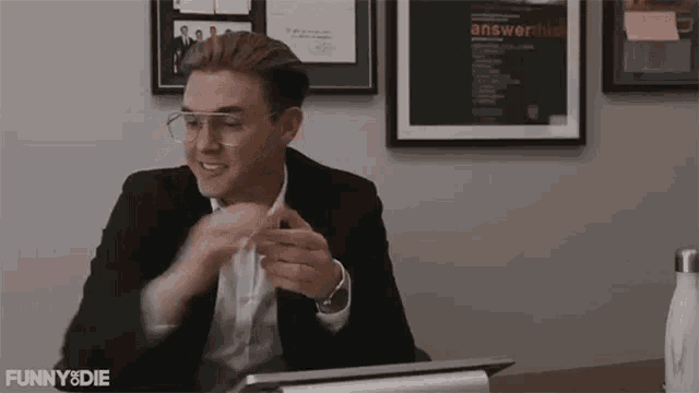 a man wearing glasses and a suit is sitting at a desk .