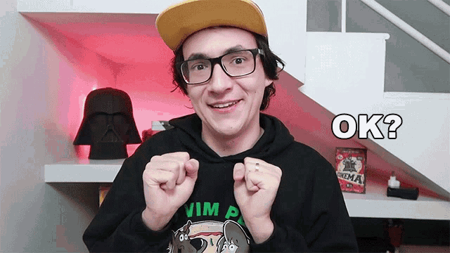 a young man wearing glasses and a yellow hat says " ok "