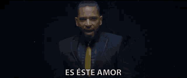 a man in a suit and tie stands in front of a black background that says es este amor