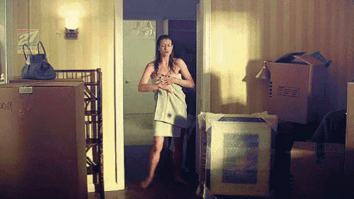 a woman is wrapped in a towel in a room with boxes and a sign that says 27 on it