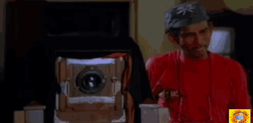 a man in a red shirt is standing in front of a large camera
